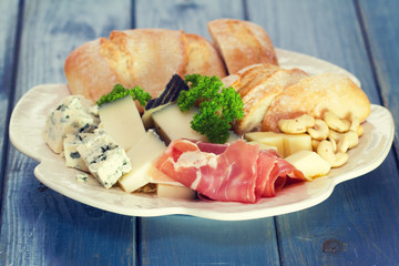 prossiutto with cheese and bread on white plate on blue wooden background