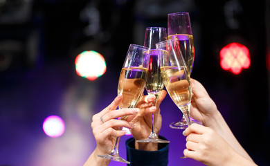 Clinking glasses of champagne in hands on bright lights backgrou