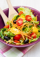 mixed salad with tomatoes in purple bowl on wood table