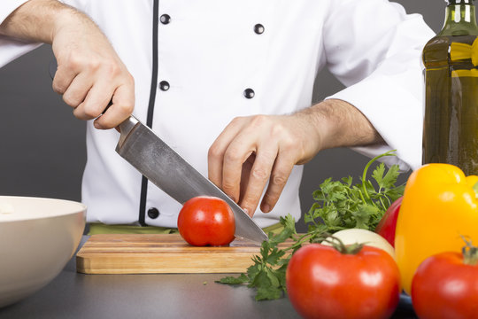 Chef's hands cutting red fresh tomato