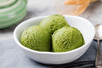 Green tea matcha ice cream scoop in white bowl on a grey stone background