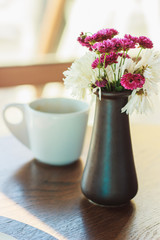 Vase with flowers and cup of coffee