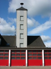 Schlauchturm mit Sirene am Feuerwehrhaus der freiwilligen Feuerwehr mit roten Industrietoren bei...