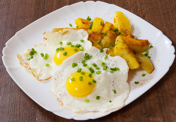 fried eggs with potato in a plate on wooden table