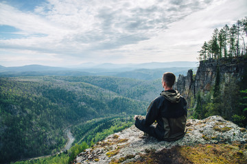 Man sitting on the top of the mountain and contemplates amazing and beautiful view of the valley