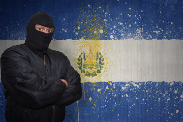 dangerous man in a mask standing near a wall with painted national flag of el salvador