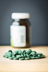 Spirulina supplement pills spread on wooden board and bottle. Antioxidant nutrition.