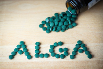 Spirulina supplement pills making up the word alga on wooden board and bottle. Antioxidant alga nutrition.