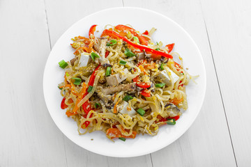 Plate of stirred rice noodles with tofu, vegetables and shiitake on a table. Traditional Asian cuisine meal. Top view.