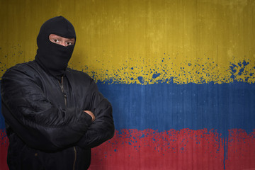 dangerous man in a mask standing near a wall with painted national flag of colombia