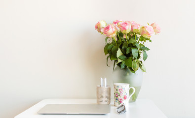 Desk with computer, cup, glasses, pens in pen holder and vase of pink roses