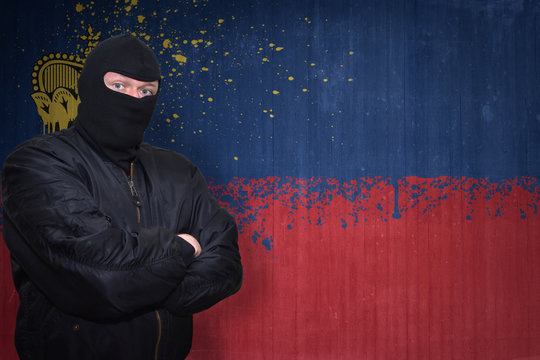 dangerous man in a mask standing near a wall with painted national flag of liechtenstein