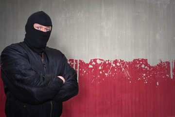 dangerous man in a mask standing near a wall with painted national flag of poland