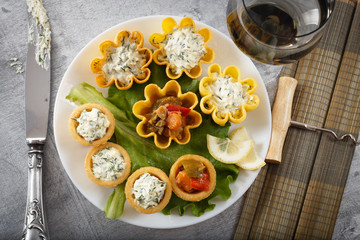 Tartlets filled with vegetables and cheese and dill salad on white plate and leaf against rustic wooden background