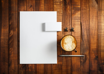 Photo of blank stationery set. Blank corporate identity template on vintage wooden table background. Letterhead, business cards, coffee cup and pen. Top view.