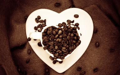 Heart shaped cup with coffee beans on brown