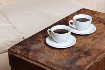Two espresso coffees in small white cups resting on the wood background