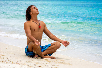 Young guy sitting in meditation pose on the beach