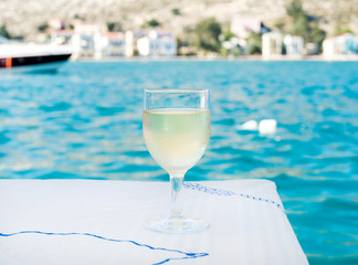 Glass of white wine on table in beach restaurant with sea view, blue water and yacht at background