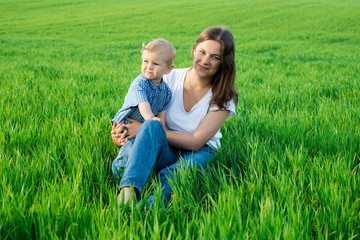 Naklejka na ściany i meble Mother and child having fun sitting on the green grass