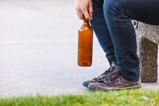 Man depressed with wine bottle sitting on bench outdoor