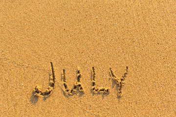 July - word inscription on the gold sand sea beach.