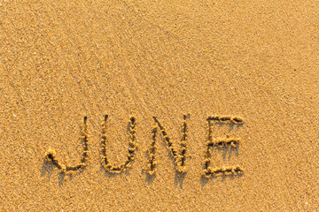 June - word inscription on the gold sand sea beach.