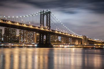 Fototapeta na wymiar New York City Manhattan Bridge over Hudson River with skyline after sunset night view illuminated with lights viewed from Brooklyn.