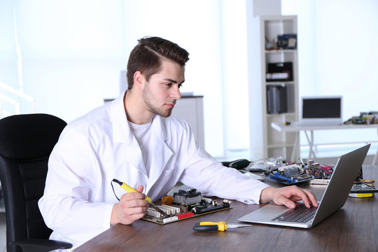 Man in white coat repairing electronic circuits in service center