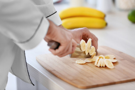 Male hands cutting banana on a wooden board.