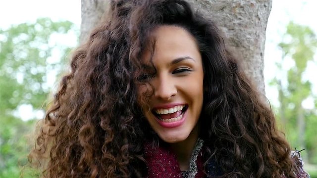 Portrait of happy young woman with beautiful curly hair smiling in a park, slow motion