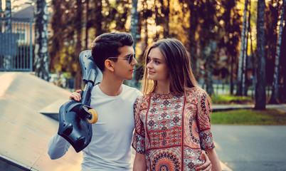Fototapeta premium Guy with skateboard and attractive young female in a park.