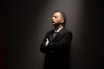 Fototapeta premium Young businessman in black suit posing with crossed or folded arms and looking away over grey background in studio.