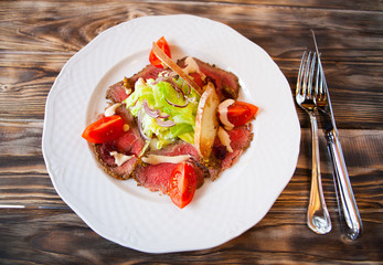Salad with slices of smoked meat and vegetables on a white plate