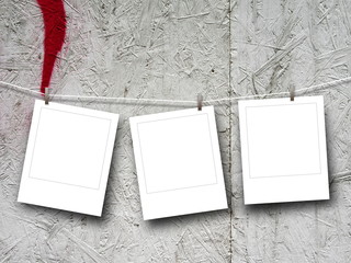 Close-up of three blank square instant photo frames hanged by pegs against painted plywood background