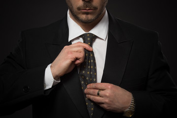 Young businessman adjusting his expensive tie isolated on grey background. Studio shot as if man is...