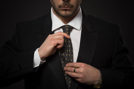 Young businessman adjusting his expensive tie isolated on grey background. Studio shot as if man is looking into mirror.