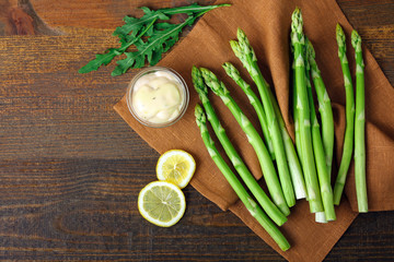 delicious asparagus with sauce and lemon slices on wooden brown background