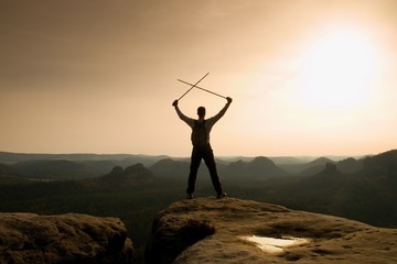 Happy hiker with x crossed poles above head.  Foggy  mountain valley bellow. Tall tourist enthusiast