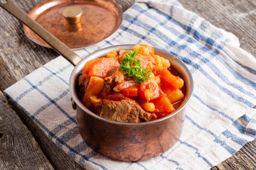 stew of beef with vegetables in a copper pot closeup