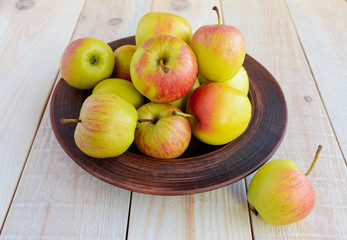 Ruddy ripe green apples in a brown bowl on a light wooden background