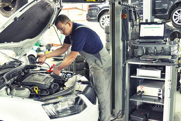 Automechaniker mit moderner Diagnosehardware bei der Reparatur der Elektronik am defekten Fahrzeug