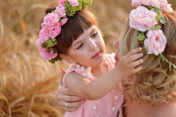 Fototapeta premium The daughter and mother look at each other, the daughter straightens the wreath of roses on her head