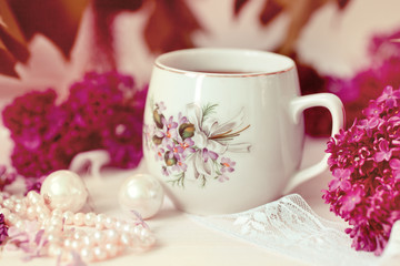 Fototapeta na wymiar a cup of tea or coffee with a pattern in lilac bouquet of lilacs