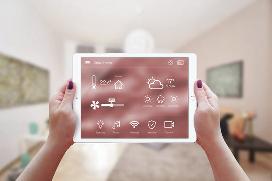 Smart remote home control app in woman hand. Living room interior in background.