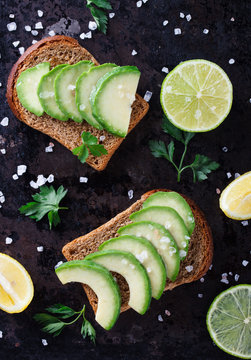 Toast with avocado on rye bread with parsley and salt on a dark background.