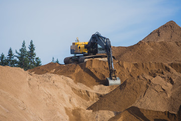 Obraz premium Yellow heavy excavator and bulldozer excavating sand and working during road works, unloading sand and road metal during construction of the new road