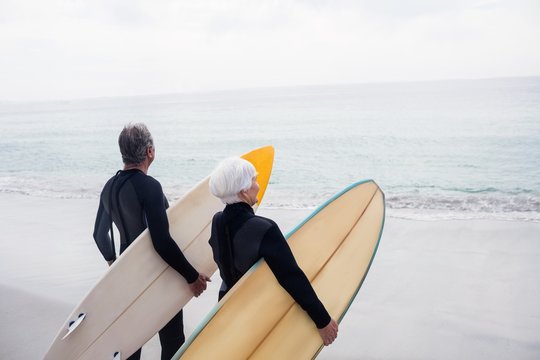 Senior couple in wetsuit holding surfboard on beach