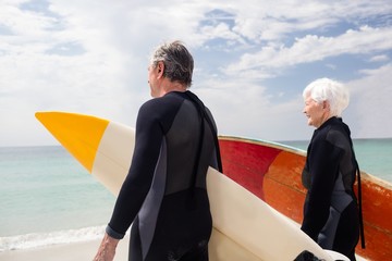 Senior couple in wetsuit holding surfboard on beach