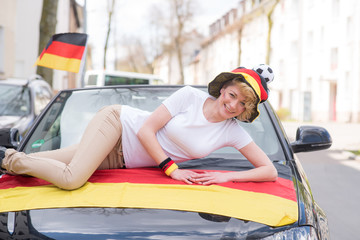 glückliche frau im deutschlandlook liegt auf motorhaube